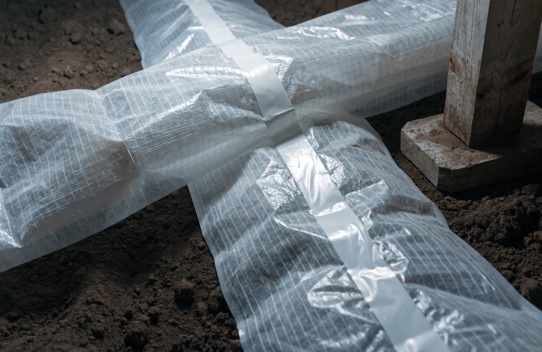 A close view of two runs of crawl space vapor liner overlapped and sealed with seam tape across bare ground